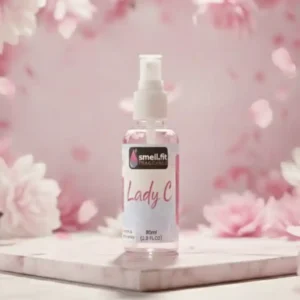 A professionally shot, high-contrast product photograph featuring a clear fragrance spray bottle with a "Lady C" label. The background is a soft pink, highly feminine, and floral setting, rendered with stark, directional lighting that highlights the product and gives a luxurious, high-end feel.