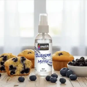 Product image of Smell.fit Fragrance 'Blueberry Muffin' 80ml (2.8 FL OZ) mist spray bottle. The bottle is surrounded by fresh blueberries, several baked blueberry muffins, and a small white bowl filled with dried blueberries, set on a rustic wooden table.