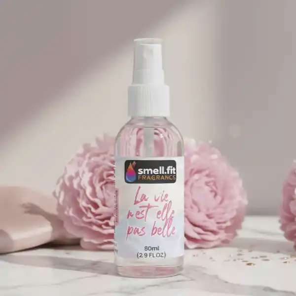 Product image of Smell.fit Fragrance 'La vie n'est elle pas belle' 80ml (2.9 FL OZ) mist spray bottle. The bottle is featured on a marble surface with large, soft-focus pink peony or rose flowers and light pink accents in the background.