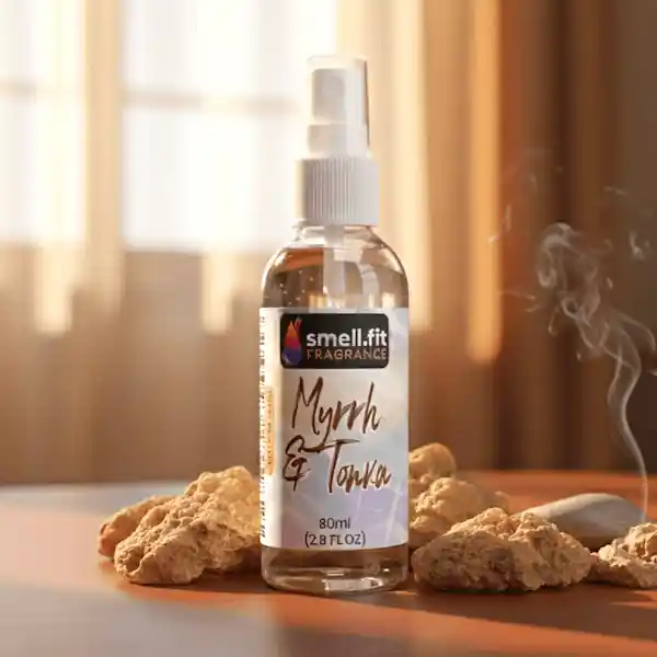 Product image of Smell.fit Fragrance 'Myrrh & Tonka' 80ml (2.8 FL OZ) mist spray bottle. The bottle is surrounded by chunks of amber or myrrh resin and a swirling plume of white incense smoke, set on a warm, brown surface near a window.