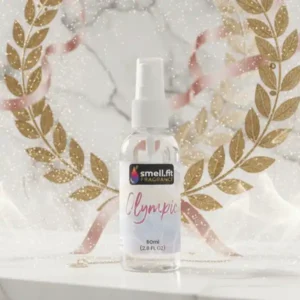 Product image of Smell.fit Fragrance 'Olympic' 80ml (2.8 FL OZ) mist spray bottle. The bottle is set on a marble surface and centered within a large, shimmering golden laurel wreath with flowing pink ribbons, evoking a feeling of victory and elegance.