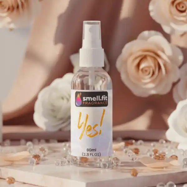 Product image of Smell.fit Fragrance 'Yes!' 80ml (2.8 FL OZ) mist spray bottle. The bottle is placed on a light marble surface and surrounded by strands of white pearls and golden beads, with soft-focus cream and blush-colored roses in the background.